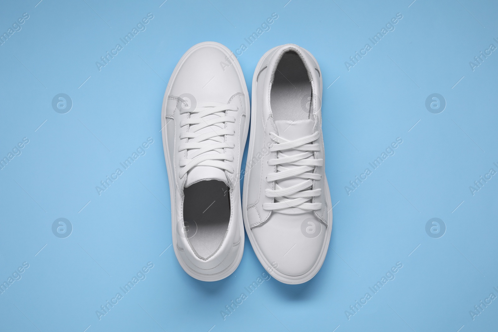 Photo of Pair of stylish white sneakers on light blue background, top view