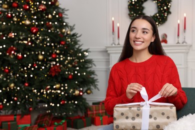 Photo of Happy young woman opening Christmas gift at home