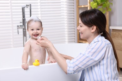 Mother bathing her cute little baby in tub at home