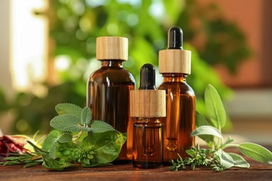 Photo of Bottles of essential oil and fresh herbs on wooden table in room