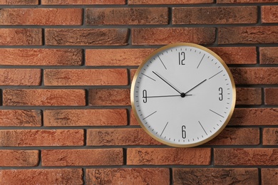 Photo of Stylish analog clock hanging on brick wall. Space for text