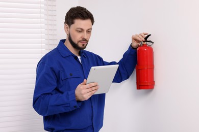 Photo of Man with tablet checking fire extinguisher indoors