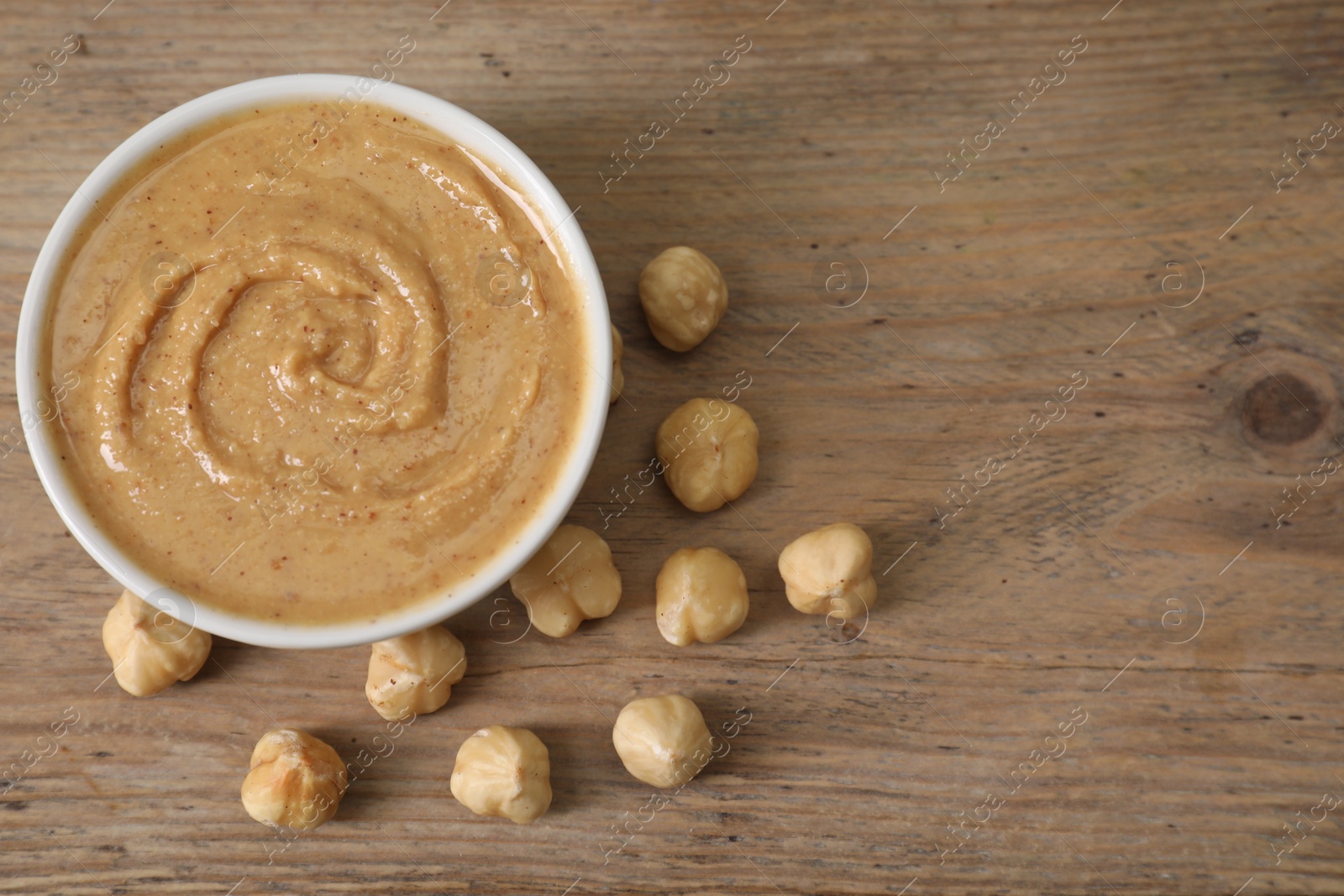 Photo of Delicious nut butter in bowl and hazelnuts on wooden table, top view. Space for text