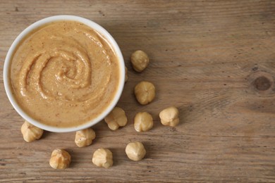 Delicious nut butter in bowl and hazelnuts on wooden table, top view. Space for text