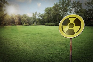 Image of Radioactive pollution. Yellow warning sign with hazard symbol near contaminated area outdoors. Space for text