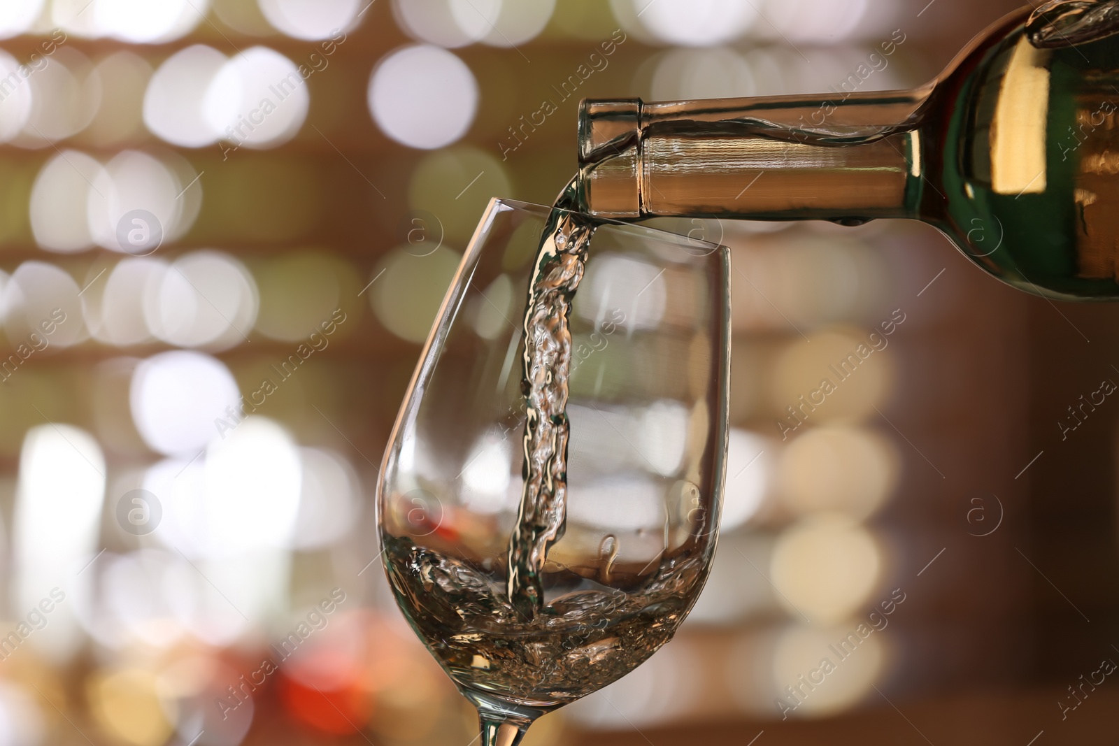 Photo of Pouring white wine from bottle into glass on blurred background, closeup