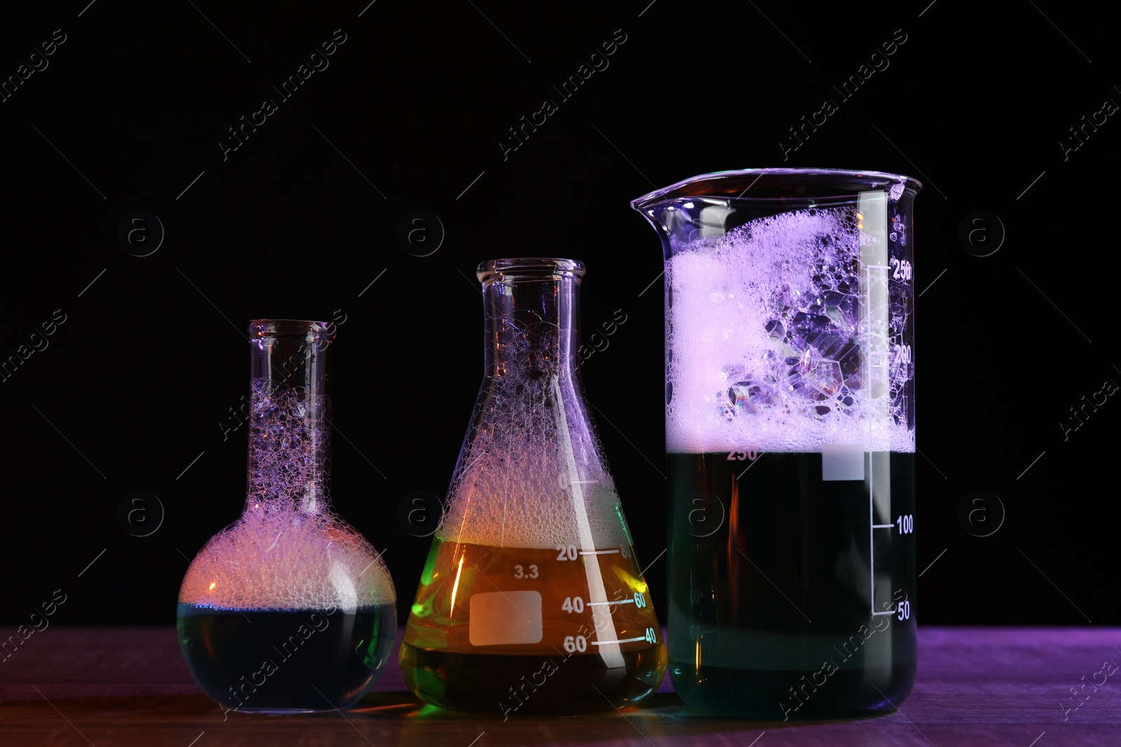 Photo of Laboratory glassware with colorful liquids on wooden table against black background. Chemical reaction