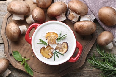 Photo of Delicious homemade mushroom soup in ceramic pot and fresh ingredients on wooden table, flat lay