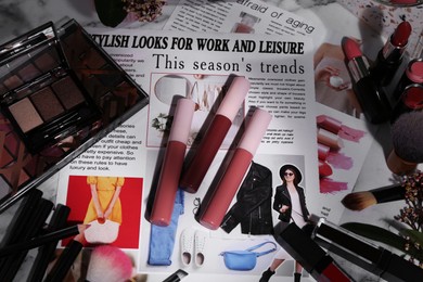 Bright lip glosses among different cosmetic products and fashion magazine on table, flat lay