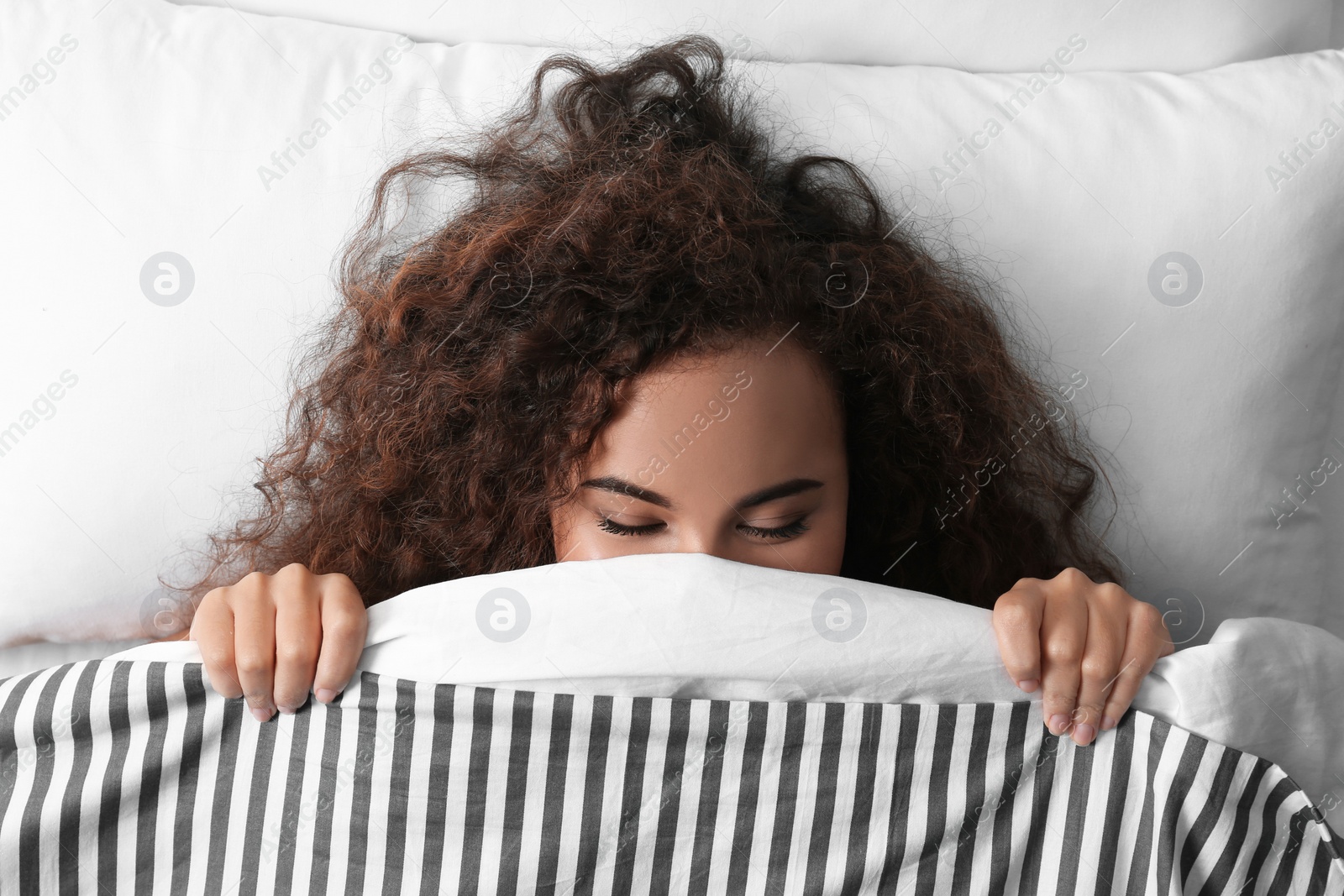 Photo of Young African-American woman sleeping on soft pillow, top view. Bedtime