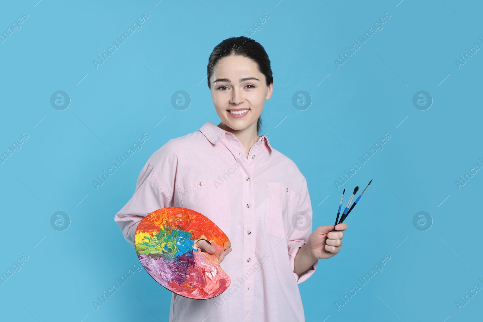 Photo of Woman with painting tools on light blue background. Young artist