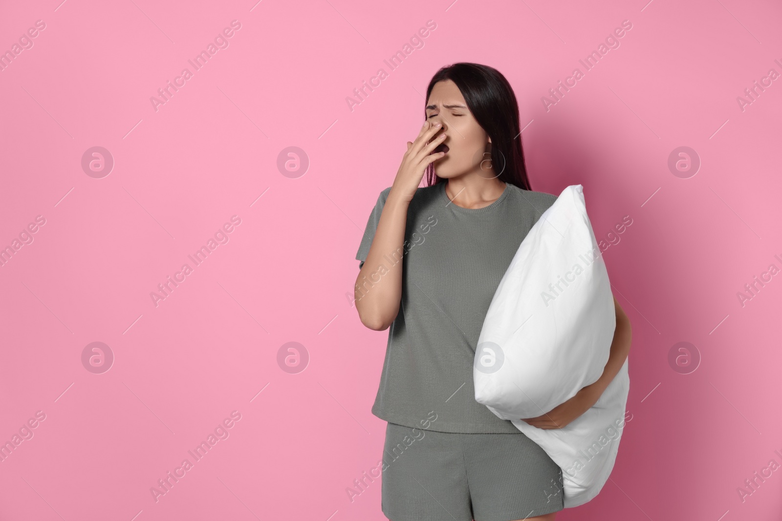 Photo of Sleepy young woman with soft pillow yawning on pink background, space for text