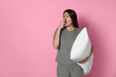 Photo of Sleepy young woman with soft pillow yawning on pink background, space for text