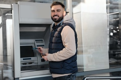 Photo of Young man with credit card near cash machine outdoors