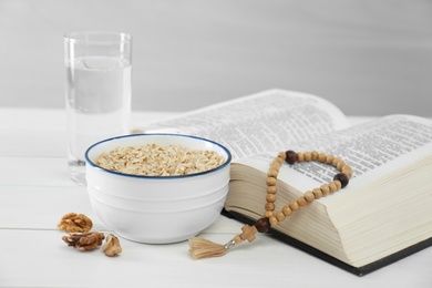 Oatmeal, rosary beads, Bible and glass of water on white table. Lent season