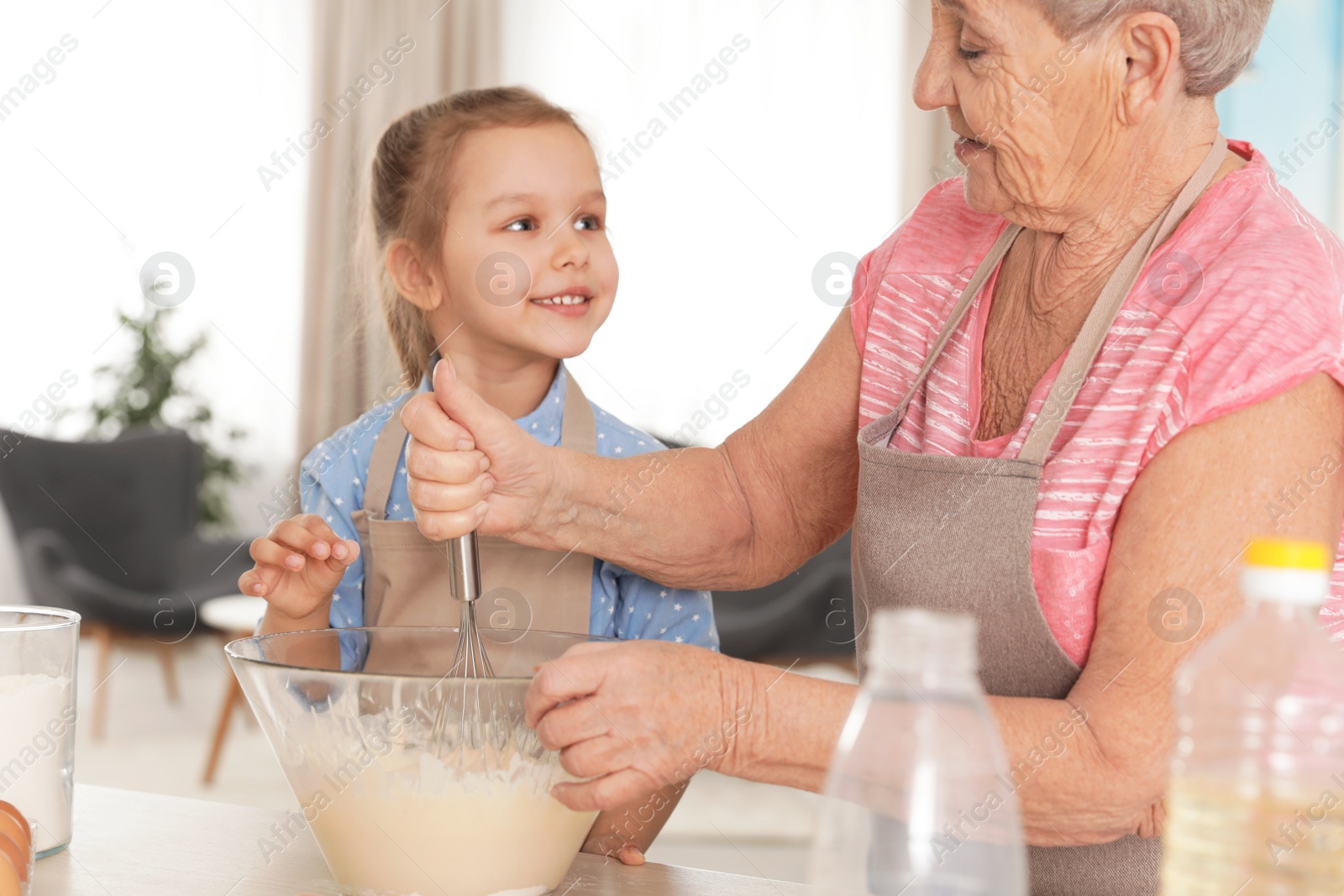 Photo of Cute girl and her grandmother cooking in kitchen