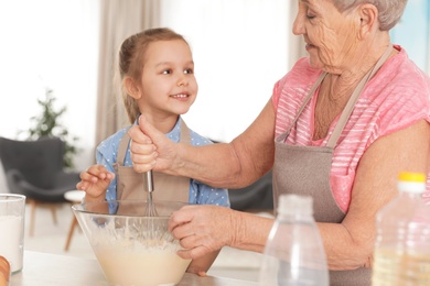 Photo of Cute girl and her grandmother cooking in kitchen