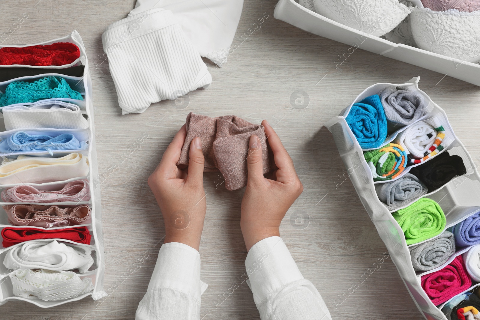 Photo of Woman rolling socks at light wooden table with organizers of underwear, top view