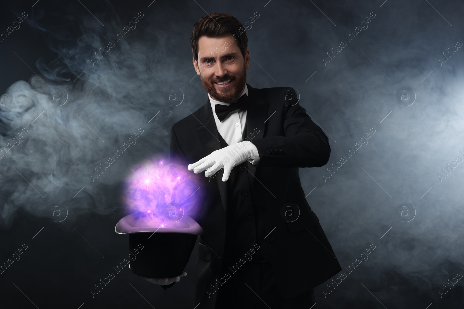 Image of Magician showing trick with fantastic light coming out of top hat on dark background