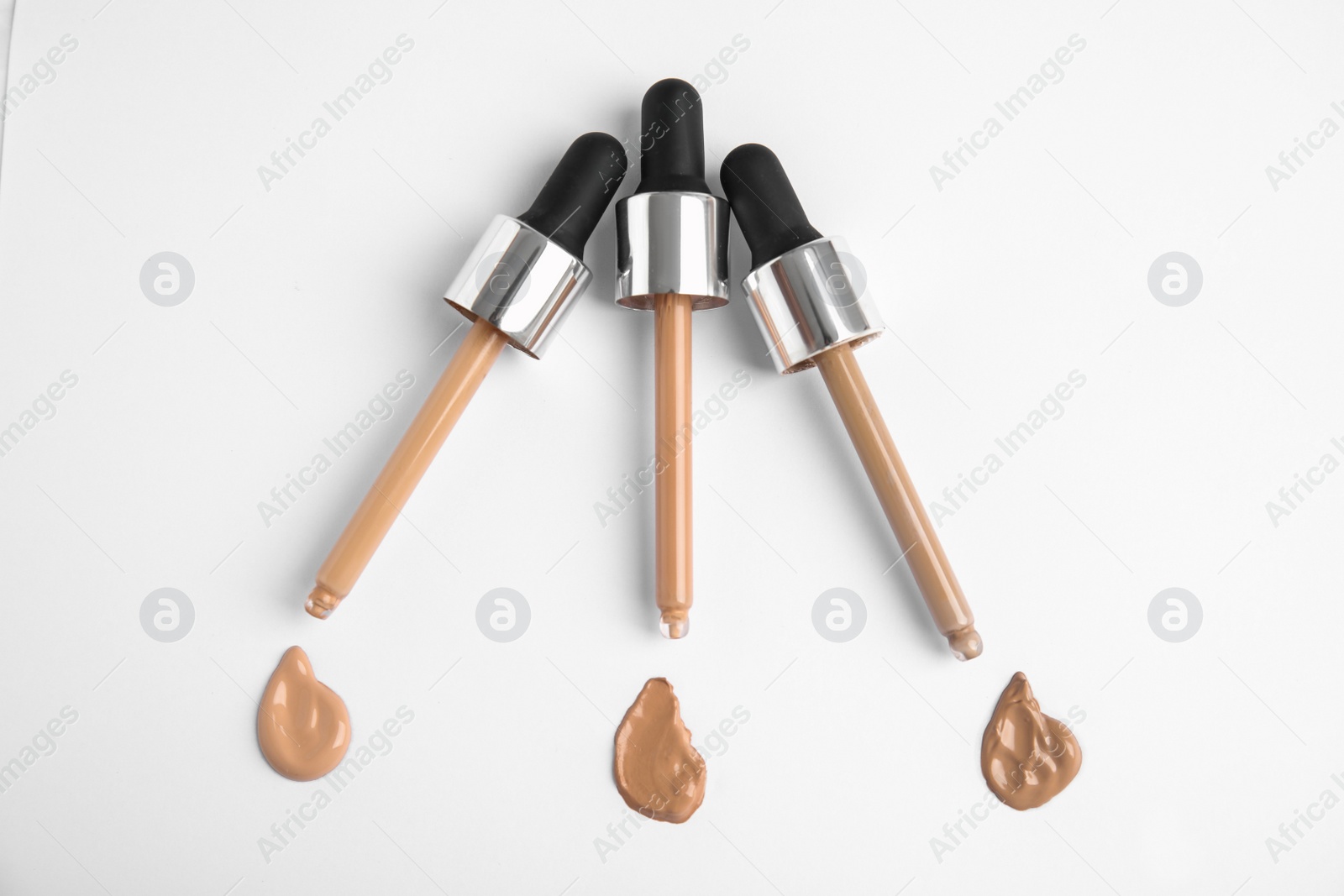 Photo of Samples of different foundation shades and droppers on white background, top view