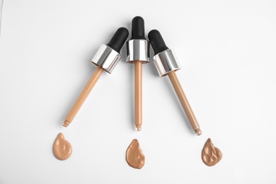 Photo of Samples of different foundation shades and droppers on white background, top view