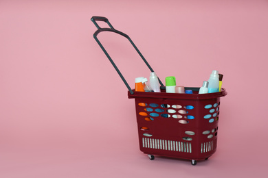 Photo of Shopping basket full of cleaning supplies on pink background. Space for text