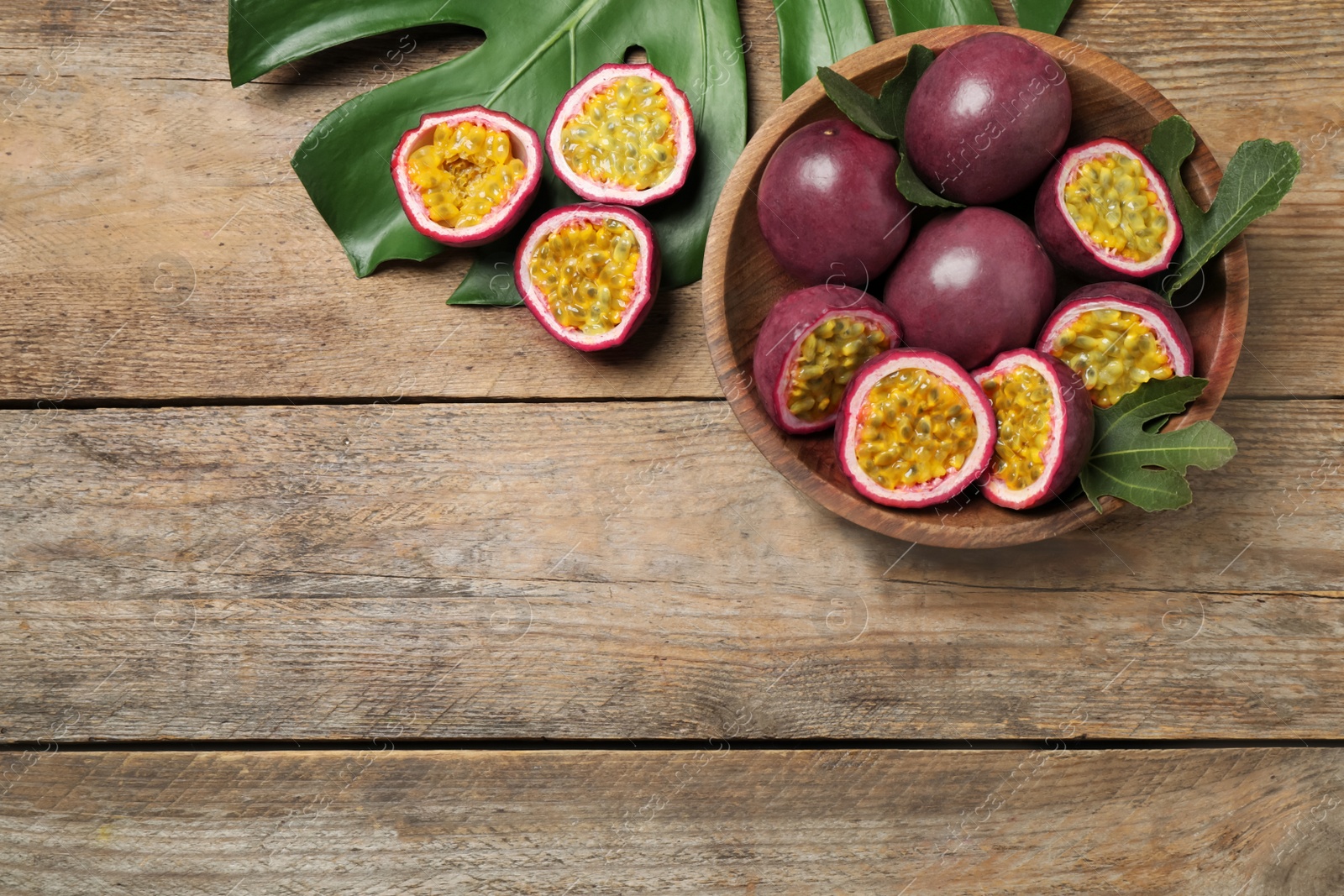 Photo of Cut and whole passion fruits (maracuyas) on wooden table, flat lay. Space for text