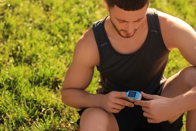 Photo of Attractive man checking pulse with blood pressure monitor on finger after training outdoors. Space for text