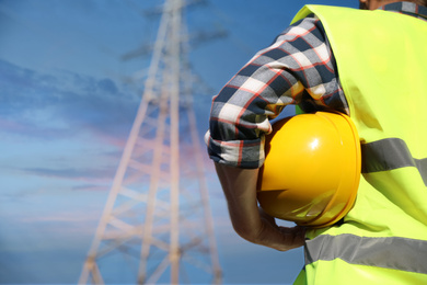 Photo of Professional electrician with helmet near high voltage tower, closeup