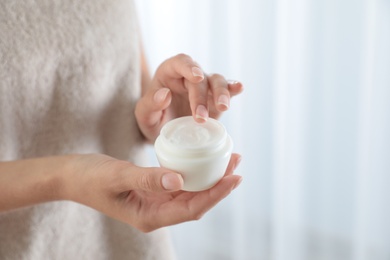 Young woman holding jar of cream at home, closeup. Space for text