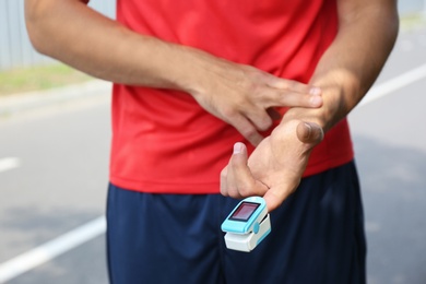 Young man checking pulse with medical device after training, closeup