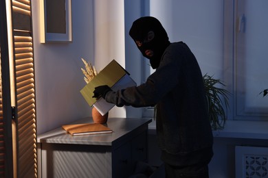 Thief wearing balaclava looking for money in foreign house. Burglary