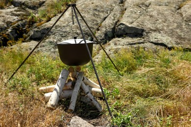 Photo of Cauldron above dry firewood arranged for bonfire outdoors. Camping season
