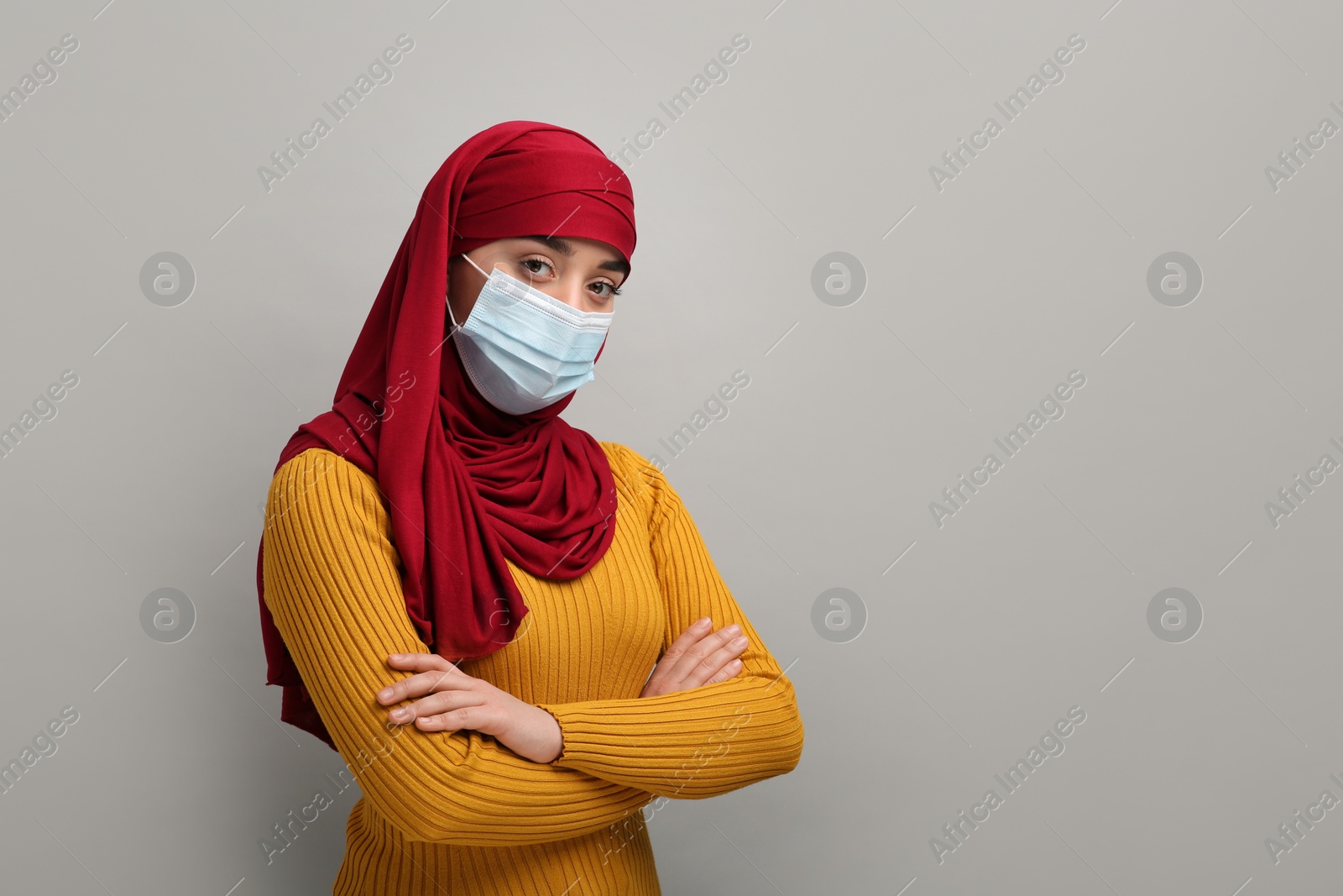 Photo of Portrait of Muslim woman in hijab and medical mask on light gray background, space for text