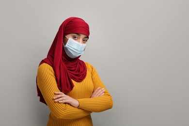 Portrait of Muslim woman in hijab and medical mask on light gray background, space for text