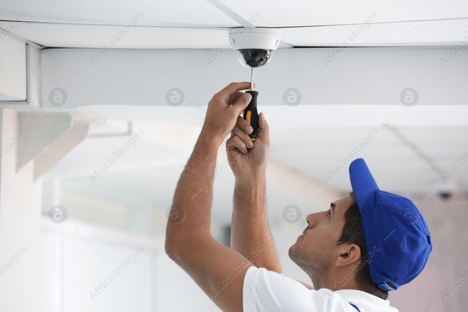 Photo of Technician installing CCTV camera on ceiling indoors