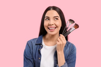 Photo of Happy woman with different makeup brushes on pink background