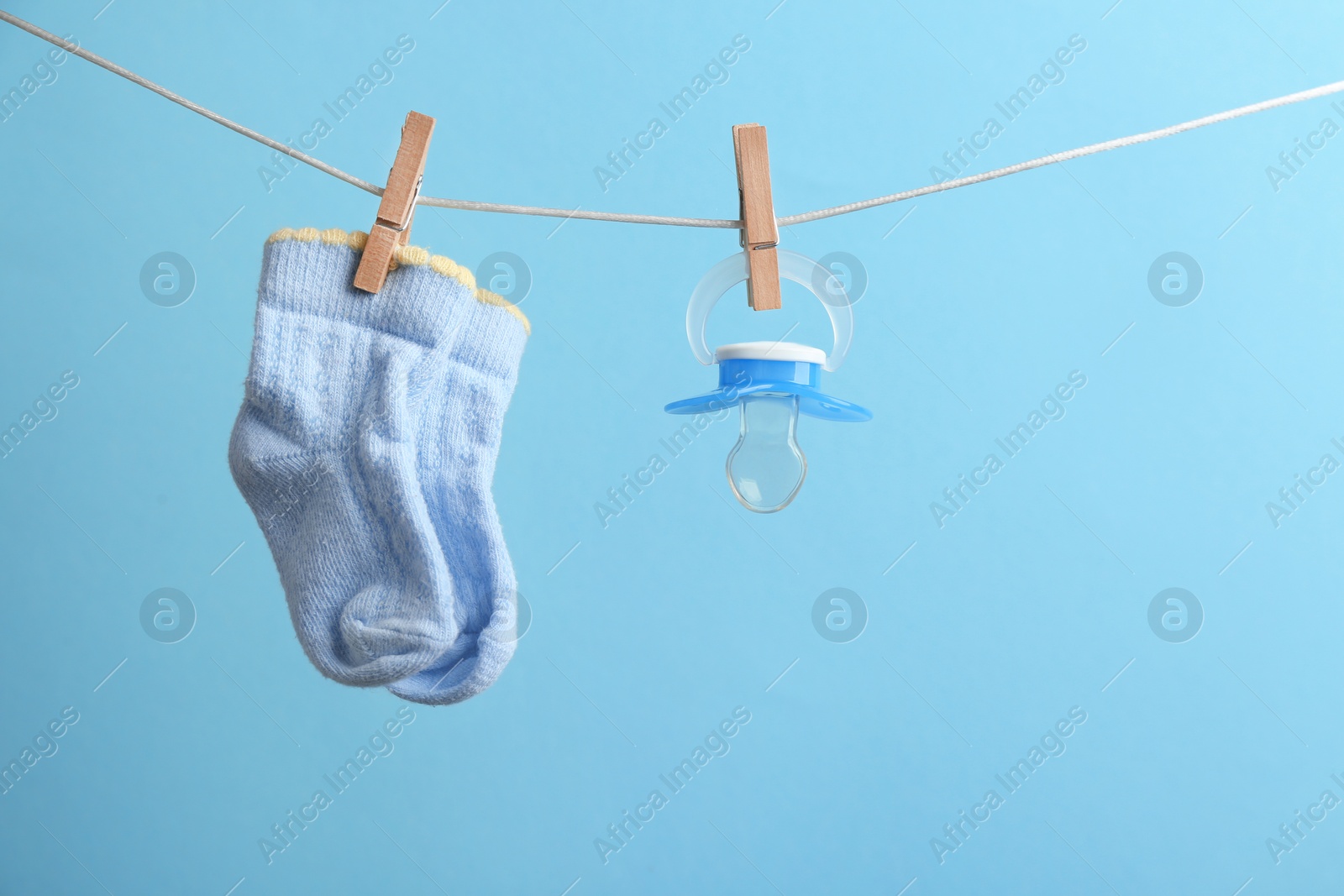 Photo of Small socks and pacifier hanging on washing line against color background, space for text. Baby accessories