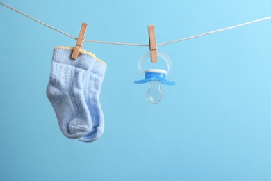 Photo of Small socks and pacifier hanging on washing line against color background, space for text. Baby accessories