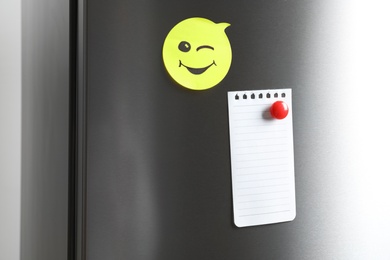 Blank note and sticker with funny face on refrigerator door. Space for text