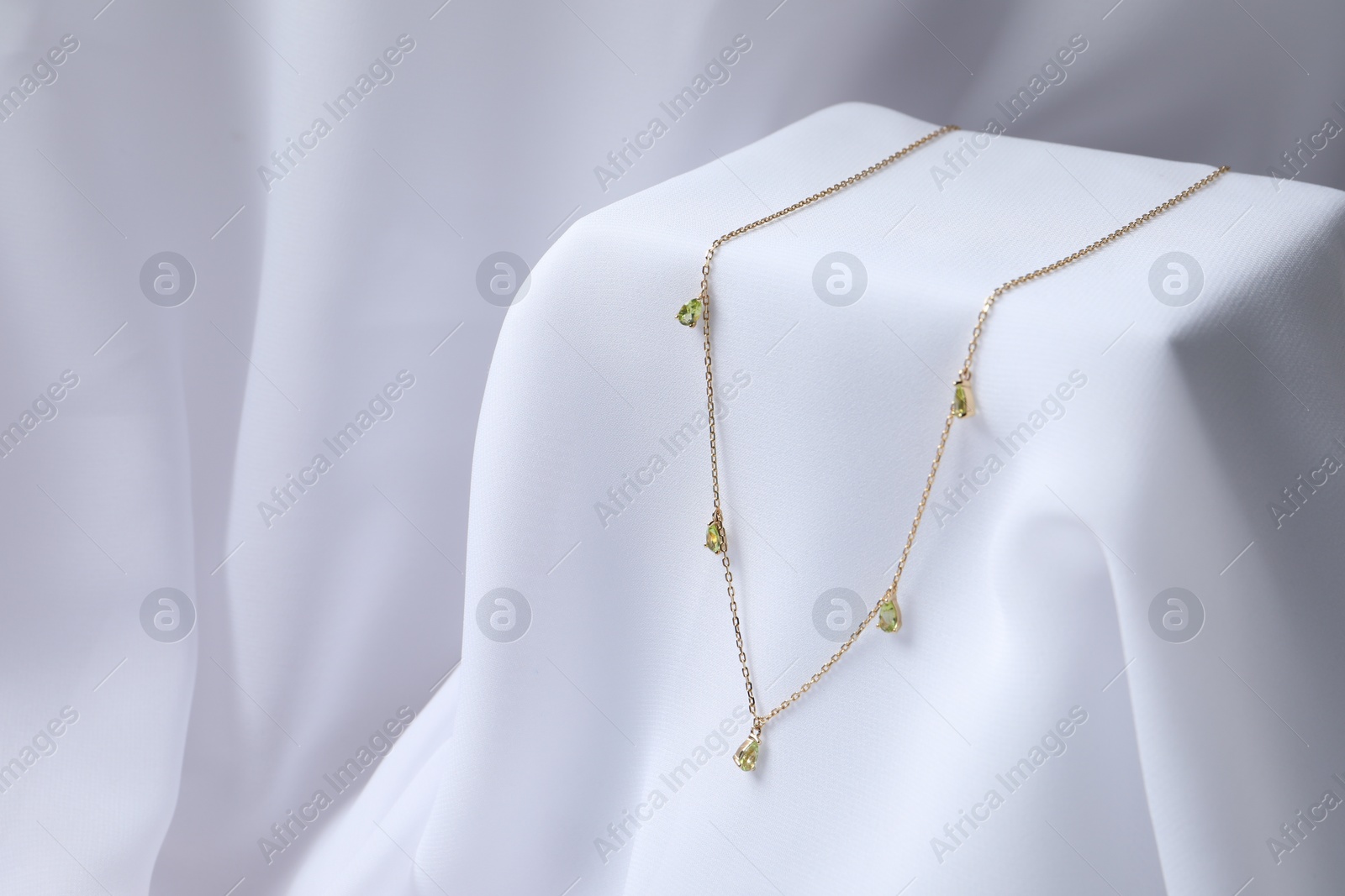 Photo of Stylish presentation of necklace on white cloth. Space for text