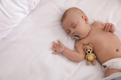 Photo of Adorable baby with pacifier and toy bear sleeping on bed, top view. Space for text