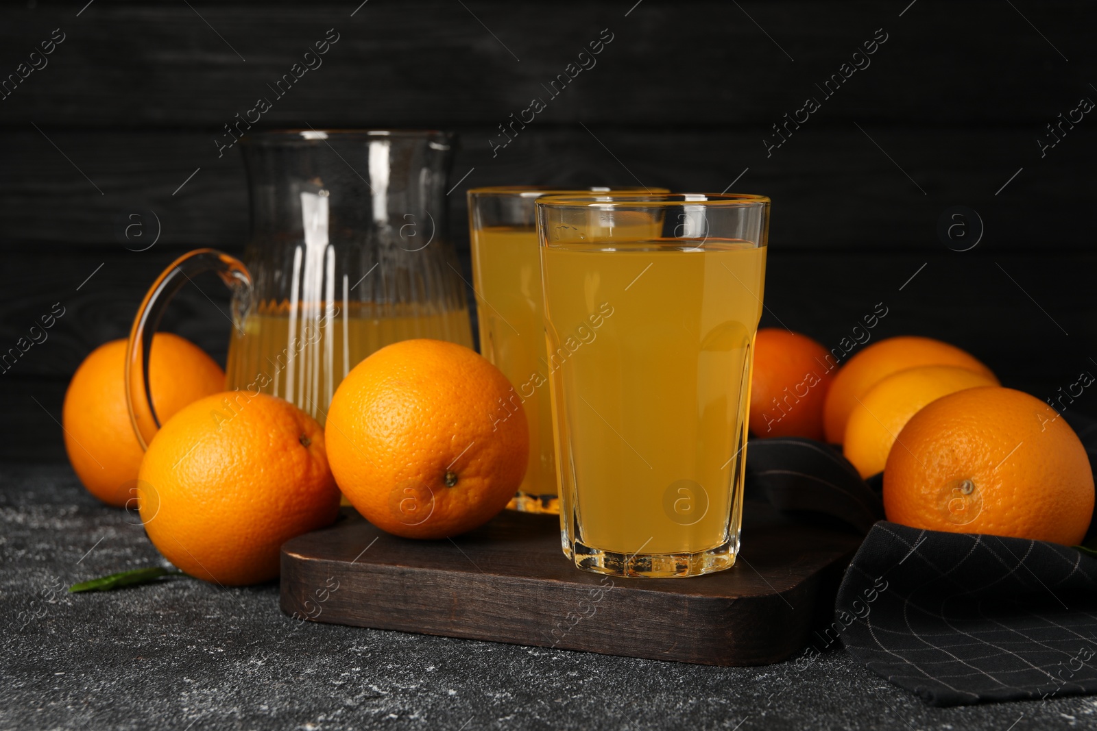 Photo of Many ripe oranges and fresh juice on dark grey table