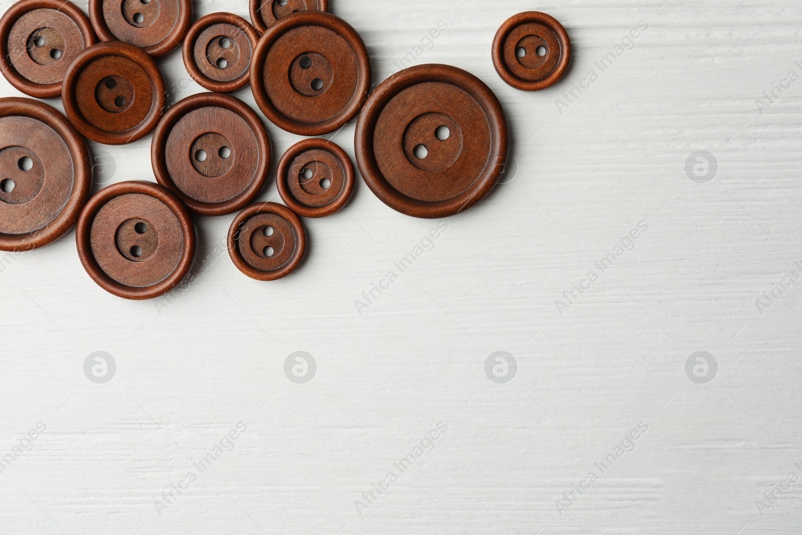 Photo of Many brown sewing buttons on white wooden background, flat lay. Space for text