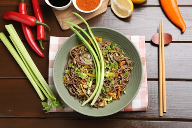 Photo of Stir-fry. Delicious cooked noodles with chicken and vegetables in bowl on wooden table, flat lay