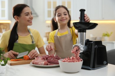 Photo of Happy family making dinner together in kitchen, daughter using modern meat grinder while mother cutting carrot