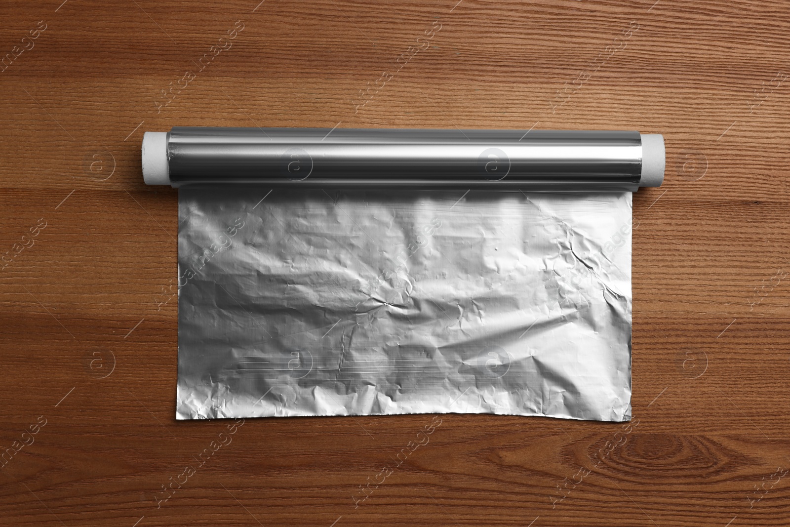 Photo of Roll of aluminum foil on wooden table, top view