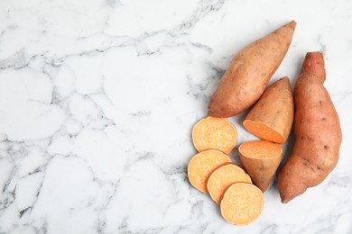 Photo of Whole and cut ripe sweet potatoes on white marble table, flat lay. Space for text