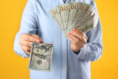 Woman holding dollar banknotes on yellow background, closeup. Money exchange concept