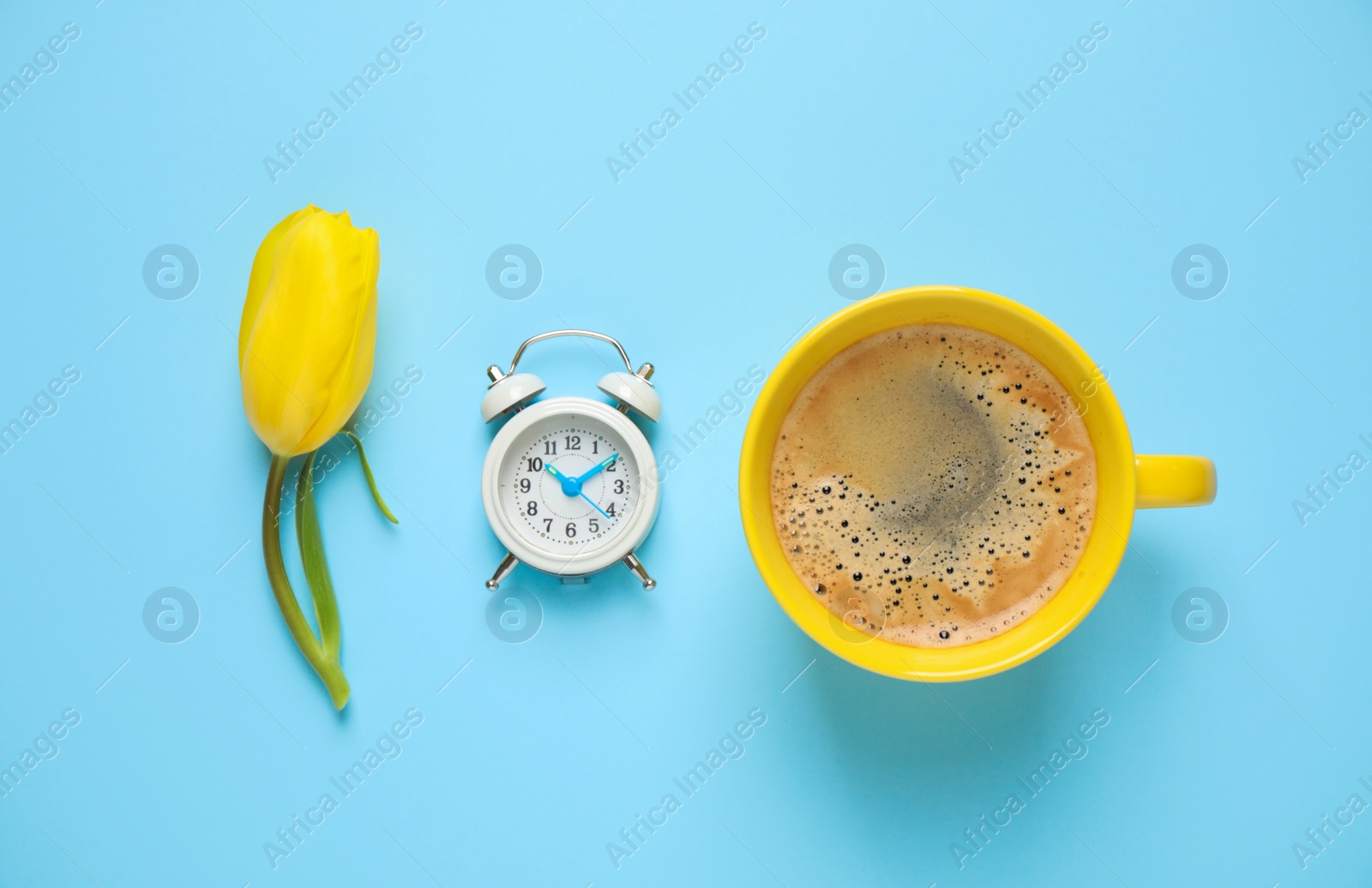 Photo of Delicious morning coffee, alarm clock and tulip on light blue background, flat lay